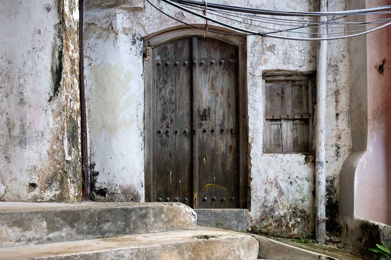 Una puerta de madera antigua, cerrada, en una calle de fachadas desconchadas.